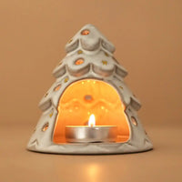 A ceramic Christmas tree-shaped tea light holder with a lit tealight candle inside, set against a warm beige background.