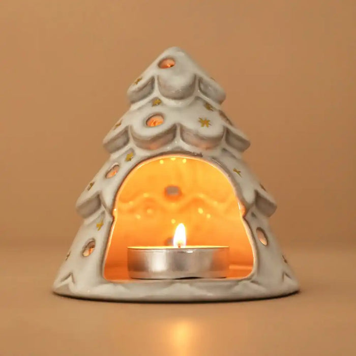 A ceramic Christmas tree-shaped tea light holder with a lit tealight candle inside, set against a warm beige background.