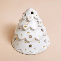 A white ceramic Christmas tree-shaped candle holder with gold star accents, set against a solid pale peach background.