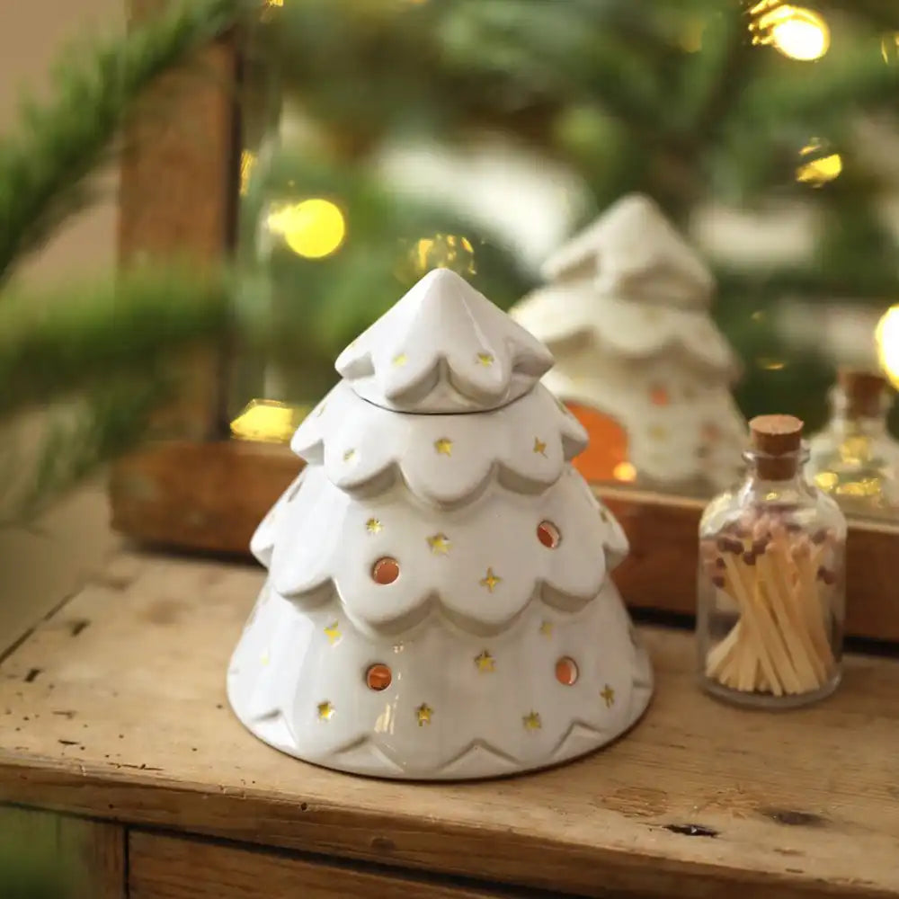 Back of white ceramic Christmas tree wax burner ornament on a wooden surface with blurred festive background