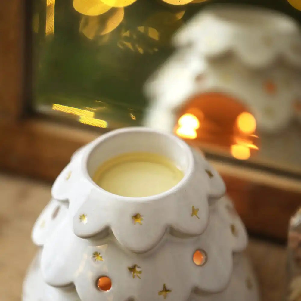 Top of white ceramic Christmas tree wax burner ornament on a wooden surface with blurred festive background