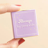 Small purple box with 'Always by your side' text held by a hand on a beige background
