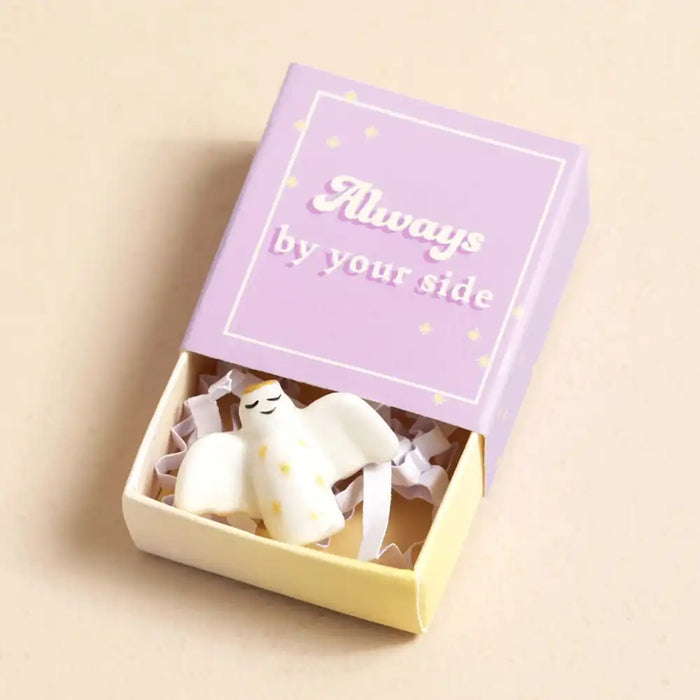 Small white figurine in a box with 'Always by your side' text on a beige background