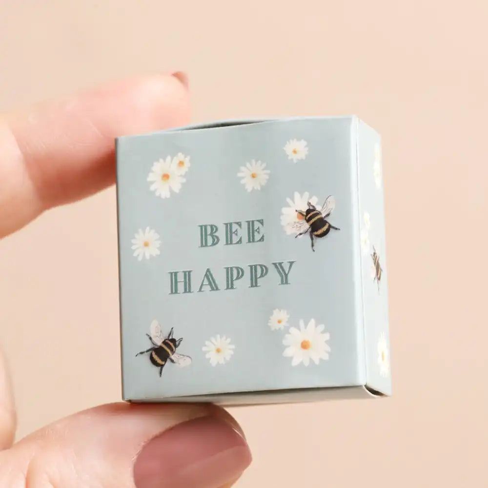 Small box with 'Bee Happy' text and bee illustrations held by a hand on a beige background