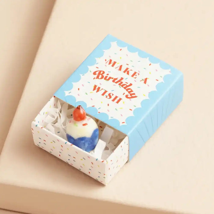 Small figurine of a birthday cake with candle in a decorative box on a beige background