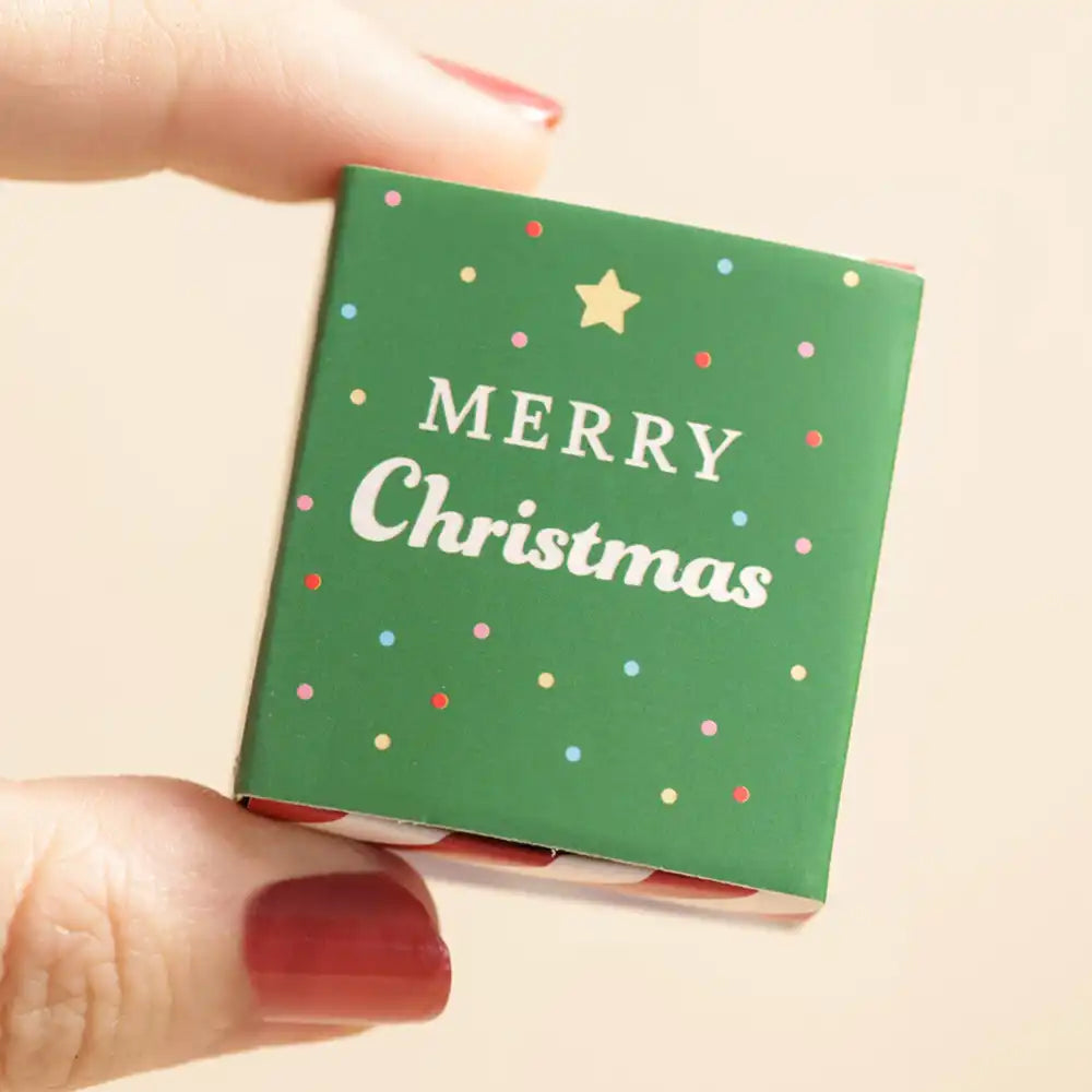 Small green box held by a hand with red nail polish on a beige background