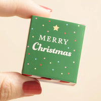 Small green box held by a hand with red nail polish on a beige background