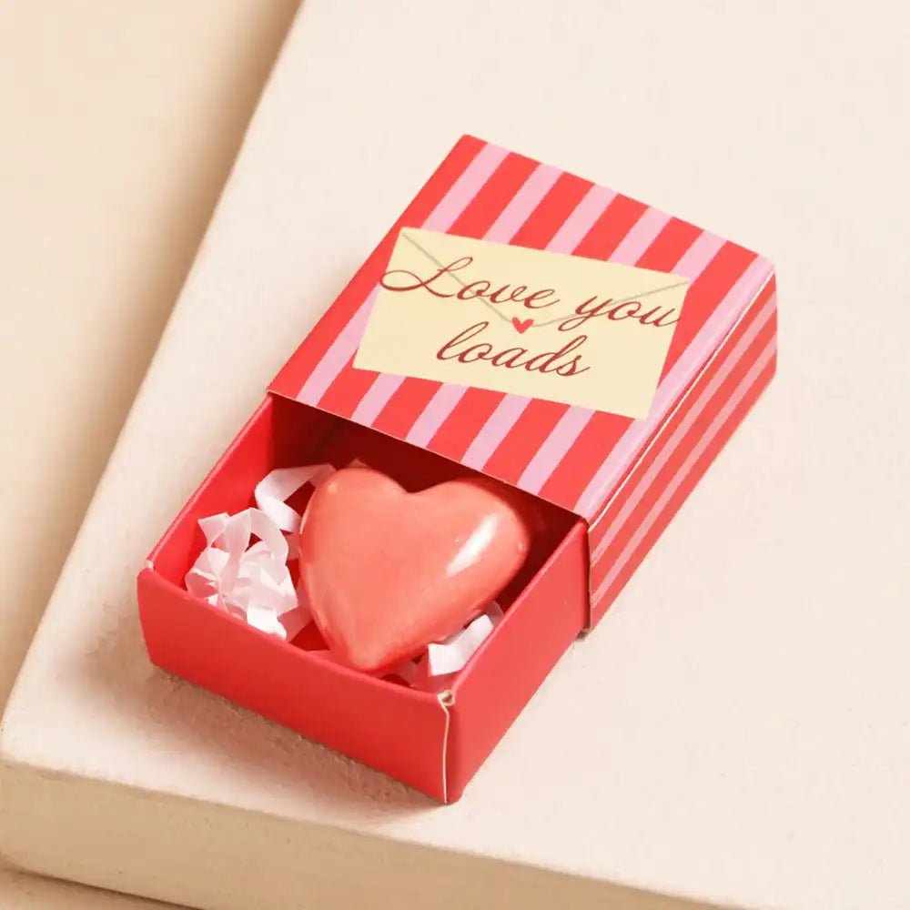 Heart-shaped ceramic token  in a red and pink striped box with 'Love you loads' text on a beige background