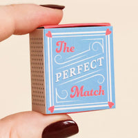 Matchbox labeled 'The Perfect Match' held between fingers against a beige background