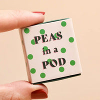 Small box with 'Peas in a Pod' text and green polka dots held by a hand against a beige background