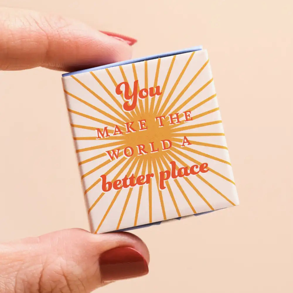 Small box with 'You make the world a better place' text held by a hand on a beige background