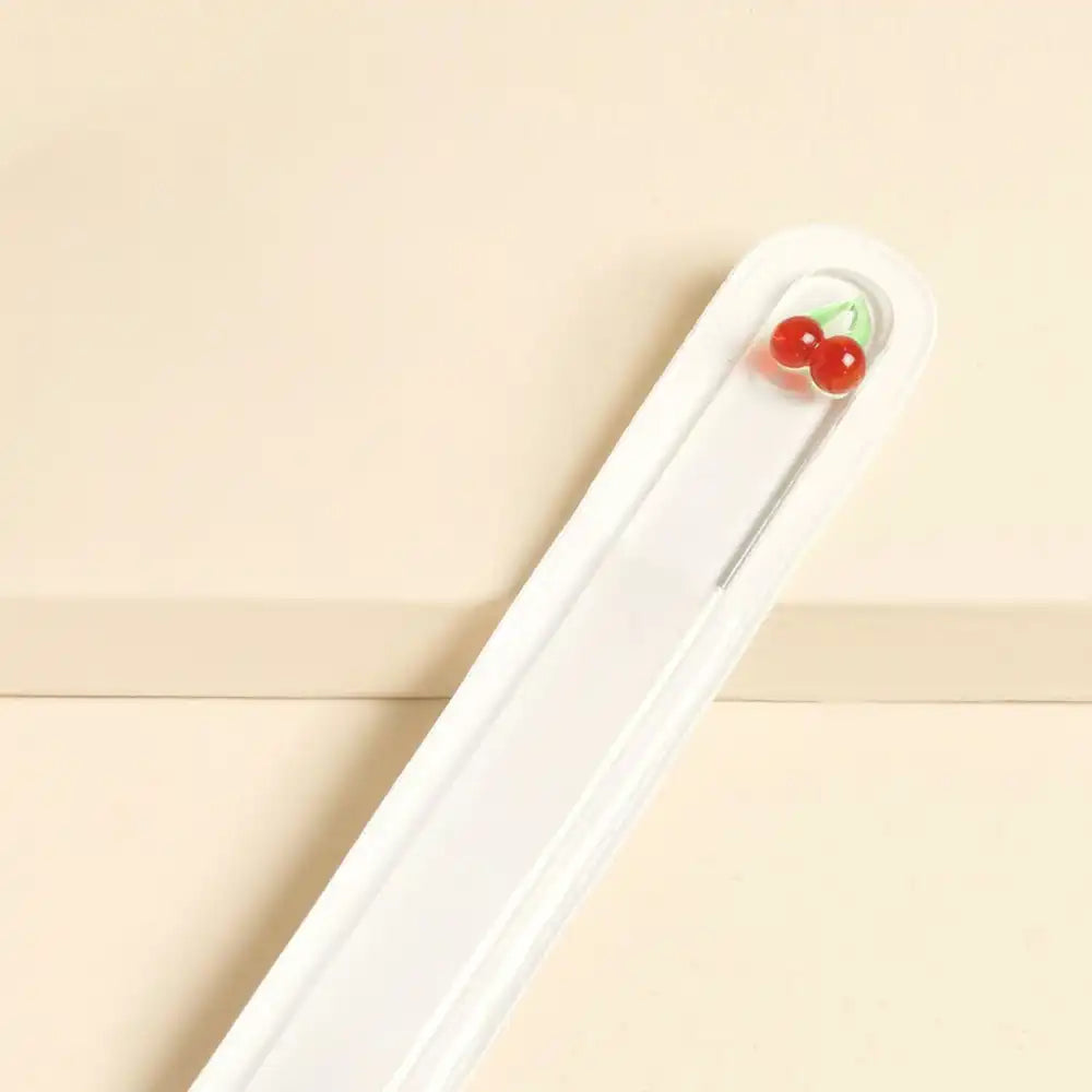 Glass nail file with glass cherry charm decoration on a beige background.