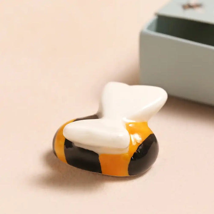 Bumblebee ceramic figurine on a beige surface with a gray box in the background