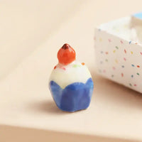 Small ceramic cake figurine with a blue base and red top on a beige surface