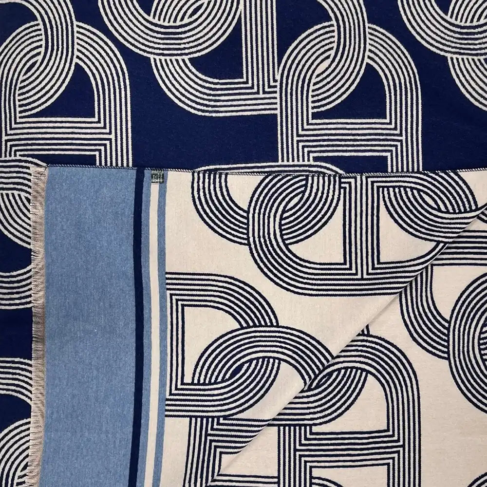 A navy blue scarf with a white geometric interlocking pattern and a light blue borde