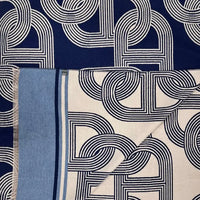 A navy blue scarf with a white geometric interlocking pattern and a light blue borde
