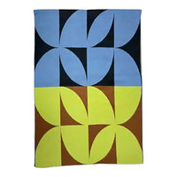 A square textile product, likely a towel or blanket, featuring a bold geometric pattern with four interlocking floral motifs. The top half is light blue on a black background, and the bottom half is lime green on a brown background.
