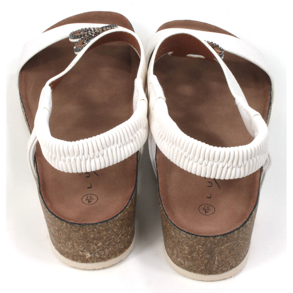 White sandals with medium cork heels. Jewelled circular decoration on the straps. Elasticated heel straps. Back view.