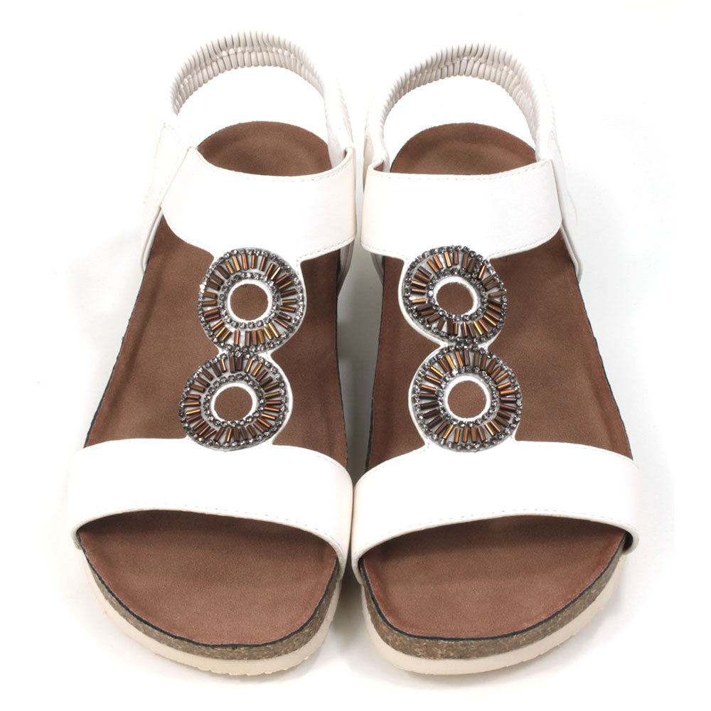 White sandals with medium cork heels. Jewelled circular decoration on the straps. Elasticated heel straps. Front view.