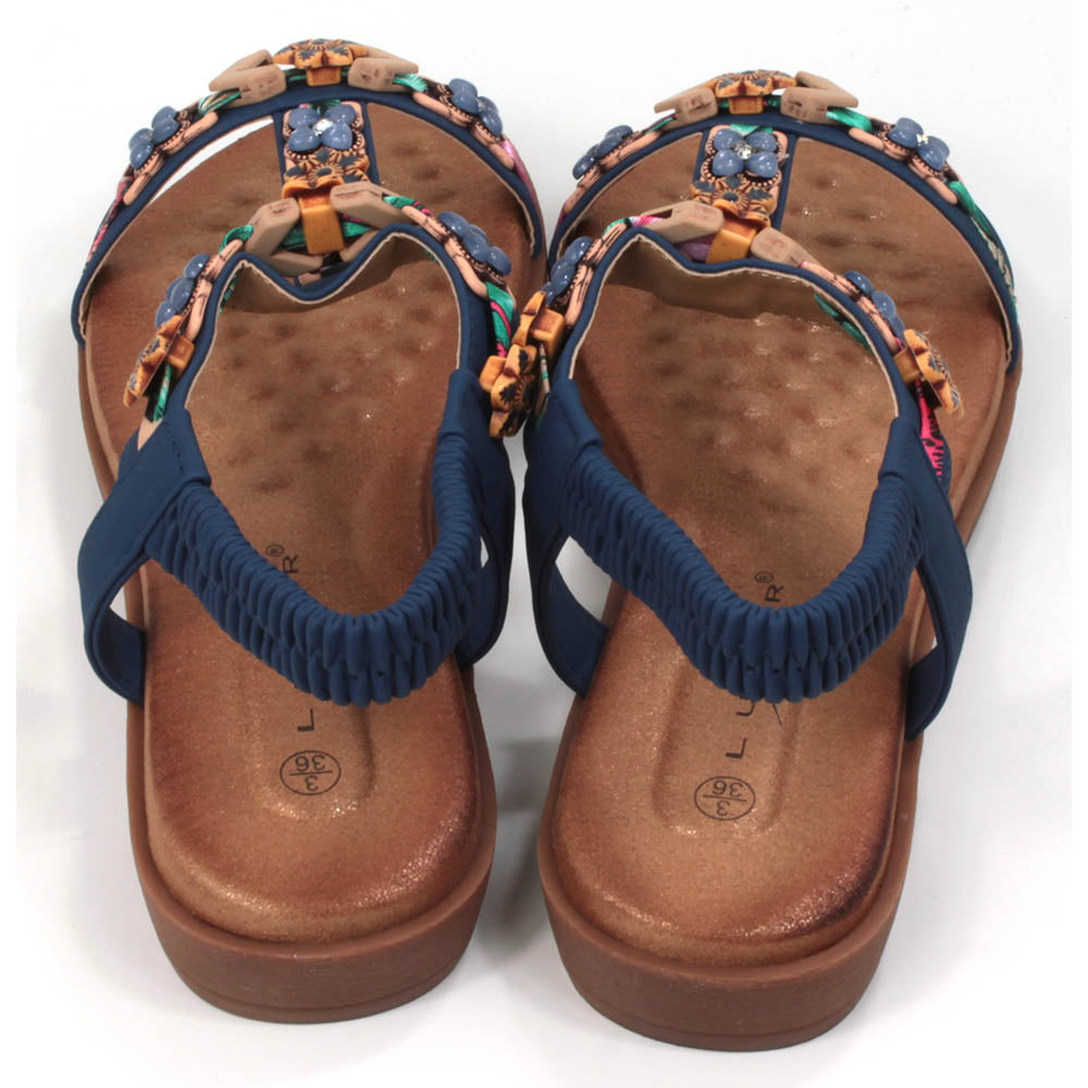 Flat sandals  with padded tan coloured footbeds. Blue straps including elasticated ankle straps.  Decorated with a large assortment of beads and other decorative elements. Back view.