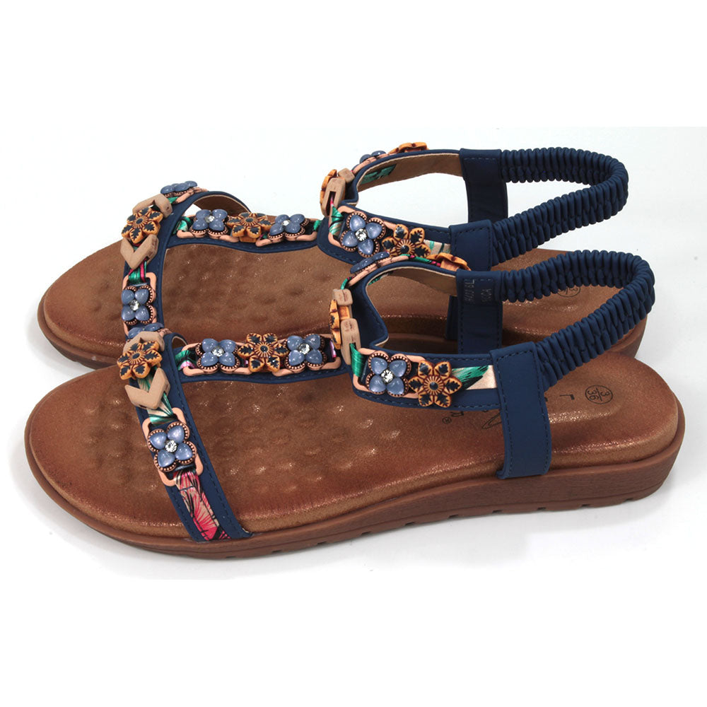 Flat sandals  with padded tan coloured footbeds. Blue straps including elasticated ankle straps.  Decorated with a large assortment of beads and other decorative elements. Side view.