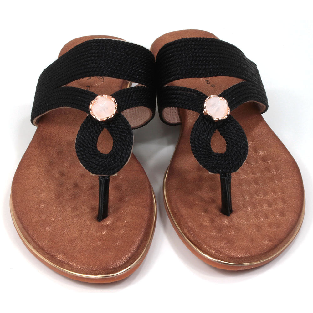 Flat toe post sandals in black with tan coloured textured footbed. Straps in textured fabric and featuring a gemstone centred over the foot. Front view.