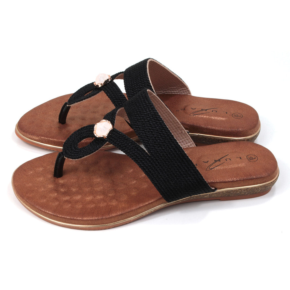 Flat toe post sandals in black with tan coloured textured footbed. Straps in textured fabric and featuring a gemstone centred over the foot. Side view.
