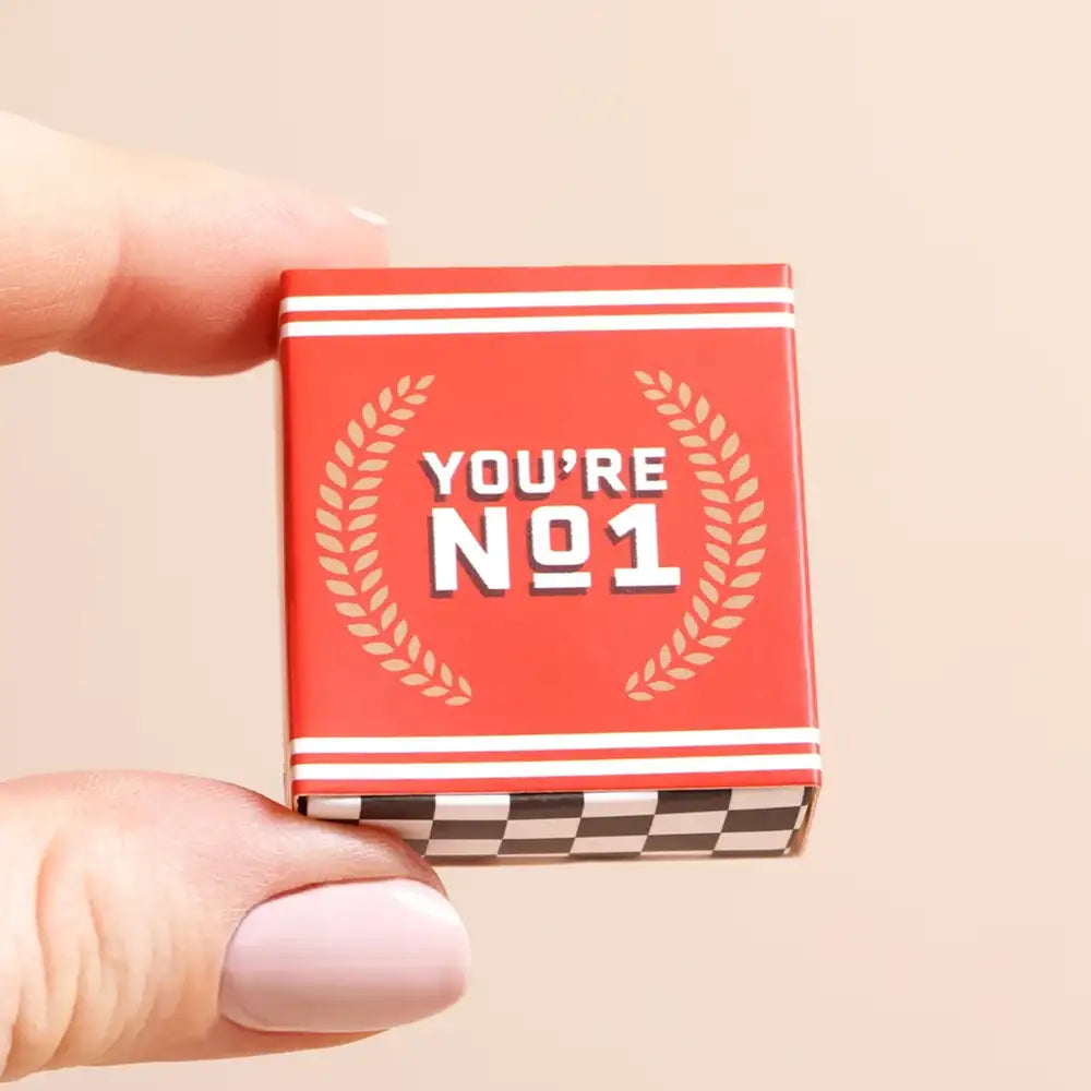 Small red box with 'You're No. 1' text held by a hand on a beige background