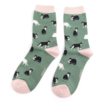 A pair of green crew socks with black and white cats and pale pink heels, cuffs and toes, shown against a plain white background.