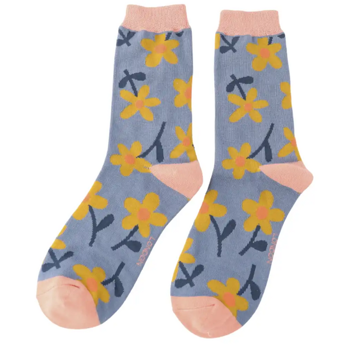 A pair of crew socks with a dusty blue background, featuring a pattern of yellow flowers with dark blue stems and leaves, and peach-colored heels, toes, and cuffs.
