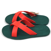 Rubber soled green flip flops. Orange rubber straps crossing the sandals in a cross over the feet. Side view.