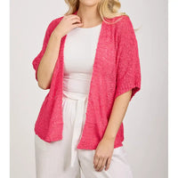 Person wearing a pink cardigan over a white top and pants on a light gray background