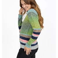 A woman wearing a fuzzy knit cardigan with horizontal stripes in green, blue, pink, and gray, paired with black pants against a plain white background.