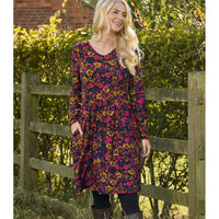 Woman wearing a floral dress standing in front of a wooden fence with greenery.