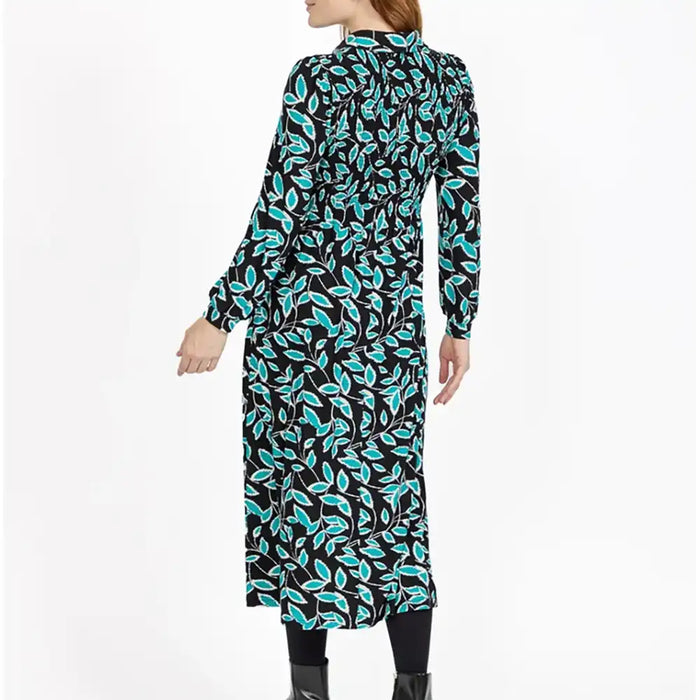 A woman modeling a long-sleeve midi dress with a black background and a vibrant turquoise and white leaf pattern, shown from a rear three-quarter view against a plain white studio background.