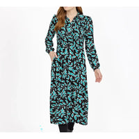 A woman modeling a long-sleeve midi dress with a black background and a vibrant turquoise and teal leaf pattern, set against a plain white studio background.
