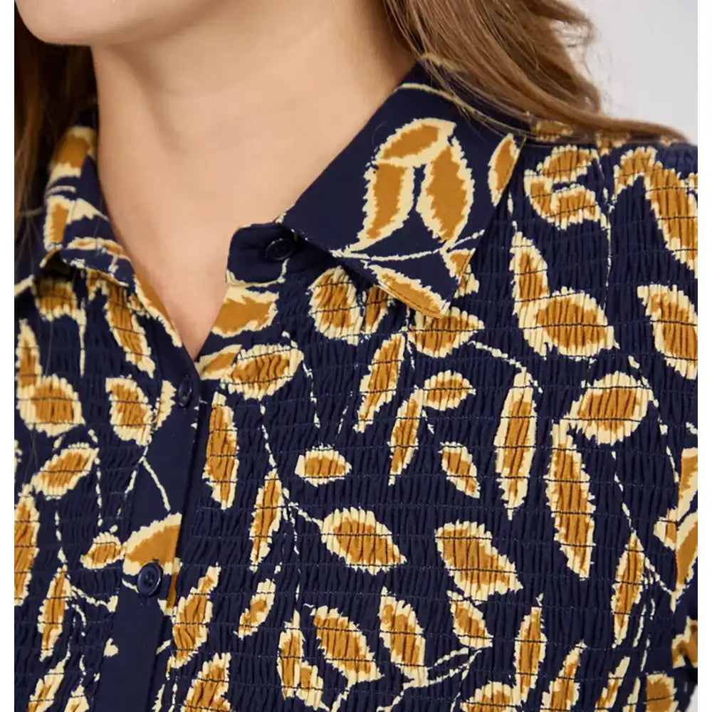 Close-up of a woman wearing a smocked button-up shirt with a navy blue base and a mustard yellow and cream leaf pattern.