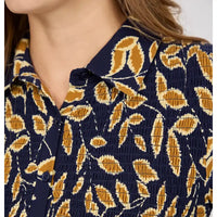 Close-up of a woman wearing a smocked button-up shirt with a navy blue base and a mustard yellow and cream leaf pattern.