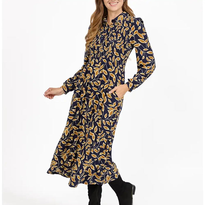 A woman wearing a navy blue long-sleeve midi dress with a mustard yellow leaf pattern, paired with black boots, against a plain white background.