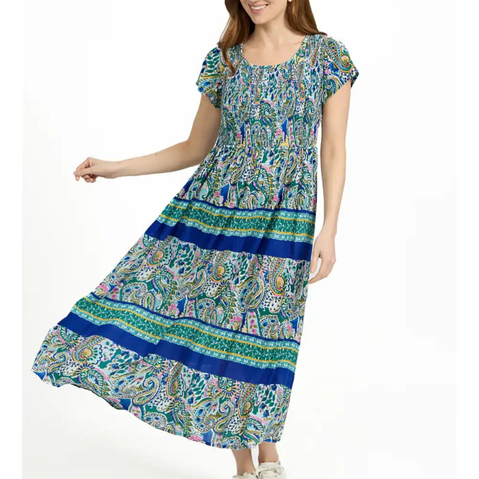 A woman wearing a short-sleeve, smocked-neck, tiered maxi dress with a colorful paisley and floral print in blue, green, pink, and white, posed against a plain white background.