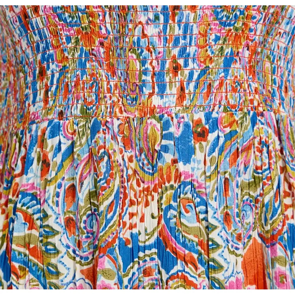 Close-up of a colorful patterned garment fabric with a smocked waistband and vertical pleats, featuring an abstract paisley-like print in blue, orange, pink, green, and white.
