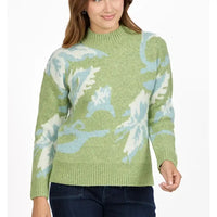 A woman wearing a light green knit sweater with a light blue and white abstract pattern, paired with dark blue jeans, against a plain white background.