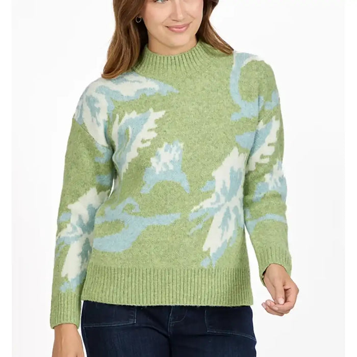 A woman wearing a light green knit sweater with a light blue and white abstract pattern, paired with dark blue jeans, against a plain white background.