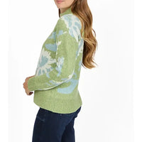 A woman wearing a light green knit sweater with a light blue and white abstract pattern, paired with dark blue jeans, shown from a side-back angle against a plain white background.