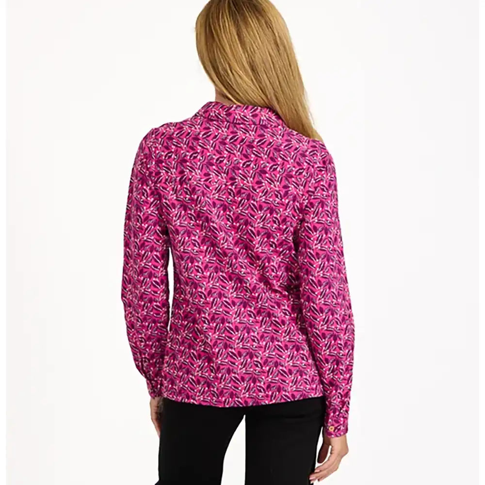 A woman viewed from the back wearing a long-sleeve collared blouse with an allover pink and magenta tropical leaf pattern, paired with black pants, against a plain white background.