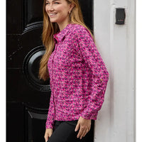 A woman wearing a pink long-sleeve button-up shirt with a white and yellow abstract pattern, standing next to a black door and a white wall.