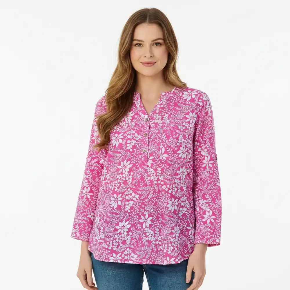 A woman modeling a pink long-sleeve button-up blouse with a white floral and botanical pattern, paired with blue jeans, against a plain white studio background.