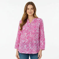 A woman modeling a pink long-sleeve button-up blouse with a white floral and botanical pattern, paired with blue jeans, against a plain white studio background.