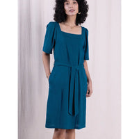 Woman wearing a teal dress against a plain background