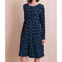 A woman wearing a long-sleeve knee-length dress with a dark navy base and a lighter blue polka dot pattern, standing against a solid beige backdrop.